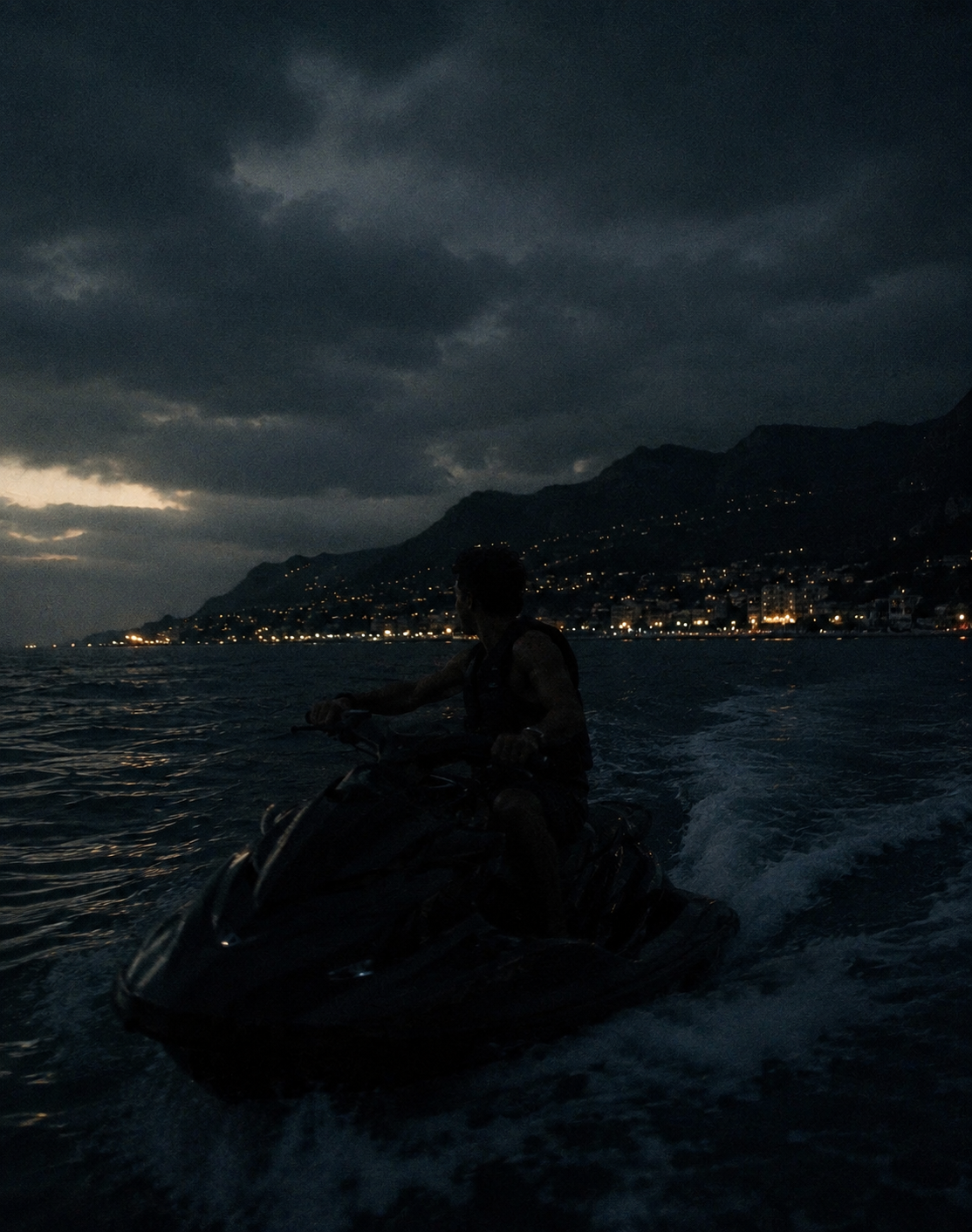 A figure on a jet ski at dusk with coastal lights and mountains in the background